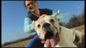 1785994439_maxresdefaultjpg - Affiliated Shops Woman smiling while posing with a large white bulldog outdoors on a sunny day, close to the camera artfully stretching toward the lens.